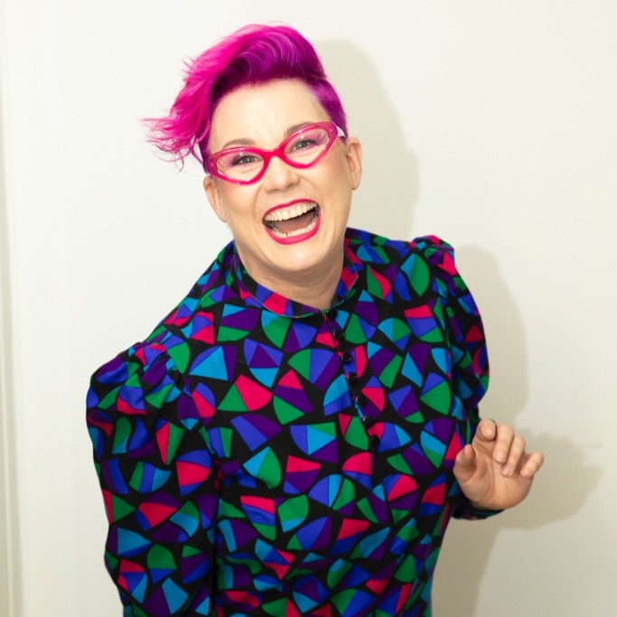 photo of Kerrie Stanley smiling with pink hair, pink glasses and  a colourful shirt.